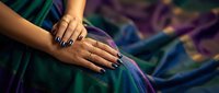 Young South Asian woman's hands with dark nail polish and gold rings resting on vibrant teal silk saree with golden border.