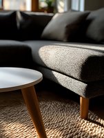 Modern living room interior with sunlight highlighting gray textured sofa, round white coffee table with wooden legs, and natural jute rug creating cozy atmosphere.
