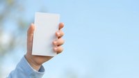 Hand holding blank white card against blue sky background, ideal for business marketing, advertising mockups, and promotional campaigns.