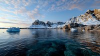Snow-covered mountain peaks rise above crystal clear arctic waters with floating icebergs reflecting in calm sea during sunset, dramatic wilderness landscape.