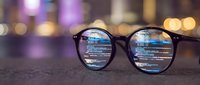 Black-framed glasses with computer code reflection on lenses against blurred city lights background. Programming, software development, coding concept.