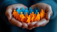 Cupped hands holding orange and blue paper cutout figures in circle representing community, unity and social support concept for business teamwork.