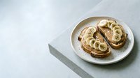 Toasted bread slices topped with creamy peanut butter and sliced bananas, served on a white plate for breakfast or snack preparation.