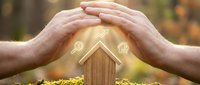 Close-up of hands protecting wooden house model with glowing icons, symbolizing home insurance, property protection, and real estate security concepts.