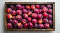 Fresh ripe red plums in rustic wooden box, top view. Organic summer fruits arranged in vintage crate, natural food photography for farm market.