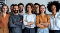 Diverse group of young professionals standing together with confident crossed arms poses, expressing unity and teamwork in modern office setting.