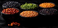 Colorful variety of raw legumes and pulses in black bowls on dark background. Red, green, yellow and black beans and lentils for healthy cooking.