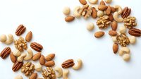 Mixed nuts and seeds scattered on white background creating natural healthy snack pattern for cooking recipes and nutrition concepts.