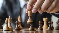 Close up of wooden chess pieces on board with hand moving queen piece, showing strategic gameplay and decision making in competitive match setting.