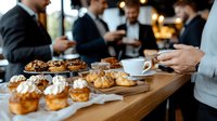 Business professionals enjoying coffee break with fresh pastries and desserts at wooden table during corporate meeting, selective focus on baked goods and coffee cup.