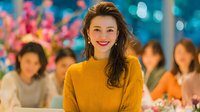 Young Asian woman in yellow sweater smiling at camera during evening celebration with friends and colorful lights in background for lifestyle content.