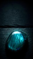 Luminous labradorite gemstone with brilliant blue-green flash on dark textured surface creating mystical atmospheric mood for spiritual wellness concepts.