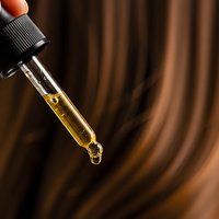Glass dropper bottle with golden oil serum against warm brown wooden background for skincare and wellness applications.
