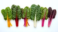 Fresh rainbow chard leaves with colorful stems arranged in gradient from yellow to purple on white background, organic leafy greens for healthy cooking.