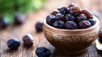Fresh dates in ornate ceramic bowl on rustic wooden table with scattered fruits for healthy snacking and Middle Eastern cuisine preparation.