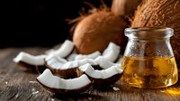 Fresh coconut pieces and glass jar of coconut oil on rustic wooden table, natural light from side creates warm ambiance for healthy lifestyle and cooking concept.