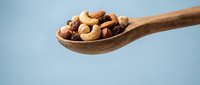 Wooden spoon filled with mixed nuts including almonds, cashews, walnuts and hazelnuts on light blue background for healthy snacking and cooking concepts.