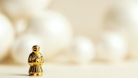 Golden bronze figurine of monk or religious figure standing on white surface against soft bokeh background for spiritual meditation concepts.