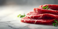 Fresh raw beef steaks with herbs on marble surface, showcasing vibrant red meat texture with white marbling for gourmet cooking preparation.