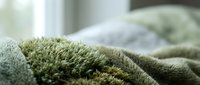 Soft green knitted wool blanket with textured surface creating cozy atmosphere in bright bedroom interior for home decor and comfort lifestyle.