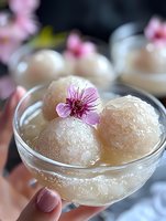 Translucent rice dumplings garnished with delicate pink cherry blossom in crystal glass bowl, traditional Asian dessert photographed in soft natural light.