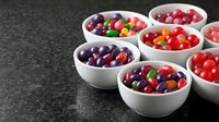 Colorful assorted candies and sweets arranged in white ceramic bowls on dark surface for confectionery display and dessert presentation.