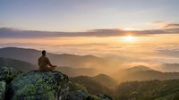 Man meditating on mountain peak at sunrise with layered hills and golden sky. Peaceful mindfulness moment in nature for wellness and spiritual growth.