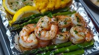 Grilled jumbo shrimp with fresh asparagus spears and lemon on aluminum foil, seasoned with herbs and spices, ready to serve seafood dinner.
