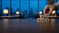 Business hand selecting wooden cube with target icon from employee blocks on office desk at night for recruitment and team building strategy.