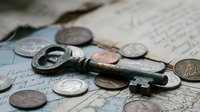 Antique skeleton key resting on vintage handwritten documents surrounded by old silver and copper coins, evoking history, mystery, and treasure.