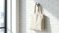 Natural cotton tote bag hanging on white brick wall hook in bright modern interior space for eco-friendly shopping and sustainable lifestyle branding.