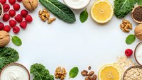 Healthy organic food frame with fresh fruits, vegetables, nuts and yogurt on white background with copy space for nutritious meal planning.
