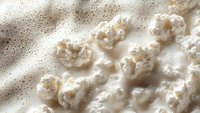Creamy white foam bubbles with soft texture and delicate shadows creating abstract pattern on light background, macro photography showing liquid soap or bath foam details.