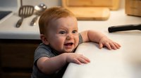 Happy Caucasian baby boy with red hair smiling while doing tummy time on white surface in modern kitchen setting for parenting and childcare content.