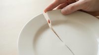 Hand placing white paper strip into clean ceramic bowl on neutral background for crafting or art project preparation.