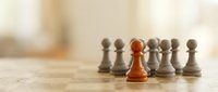 Red pawn standing out among gray pawns on wooden surface, symbolizing leadership, uniqueness, and competitive advantage in business strategy.