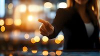 Young Asian businesswoman pointing finger against blurred city lights background with warm bokeh effect creating professional atmosphere.