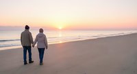 Senior couple walking hand in hand on beach at sunset, romantic golden hour moment by ocean waves, peaceful retirement lifestyle and love.