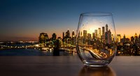 City skyline reflected in wine glass at sunset with urban lights and bridge creating romantic evening atmosphere for luxury lifestyle concepts.