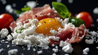 Raw egg yolk with crumbled feta cheese, prosciutto ham, fresh basil leaves and cherry tomatoes on dark background, macro food photography.