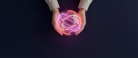 Hands holding glowing pink brain with neural network connections on dark background representing artificial intelligence and neuroscience concepts.