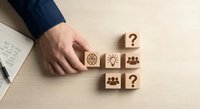 Business professional arranging wooden blocks with strategy icons including lightbulb, team, and question marks on desk for decision making concepts.