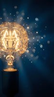 Glowing brain-shaped light bulb with sparkling bokeh effects on dark blue background representing creativity, innovation and bright ideas for business concepts.