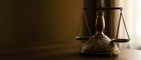 Vintage brass scales of justice on wooden desk with warm lighting creating dramatic shadows for legal and law firm concepts.