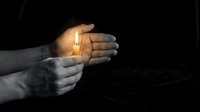 Hands holding glowing candle flame against dark background, symbolizing hope, spirituality, and light during difficult times or memorial occasions.