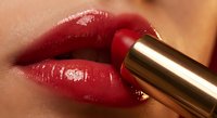 Close-up of glossy red lipstick application on full lips with golden tube, showcasing luxury cosmetics and makeup artistry for beauty campaigns.