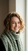 Happy young Caucasian woman with curly hair wearing green knitted scarf smiling warmly in natural light for lifestyle and fashion content.
