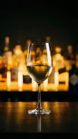 Elegant wine glass with white wine on bar counter with warm bokeh lights creating luxurious restaurant atmosphere for fine dining and hospitality concepts.