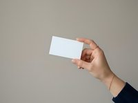 Close-up of a hand holding a blank white business card against a neutral gray background, suitable for branding, marketing, and corporate identity mockups.