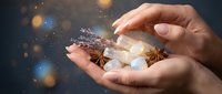 Hands holding glowing light bulb with gears and sparkles representing innovation, creativity and bright ideas for business technology concepts.